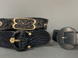 two black leather belts with gold buckles on a gray surface