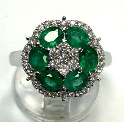 une photo d'une bague en diamant verte et blanche posée sur un socle transparent