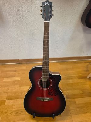 une guitare acoustique posée sur un parquet devant un mur