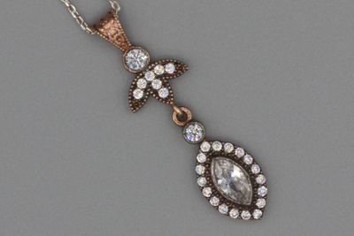 une photo représentant un pendentif en diamant suspendu à une chaîne, posé sur une surface grise