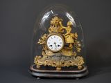 une horloge dorée sous un dôme en verre, sur fond noir