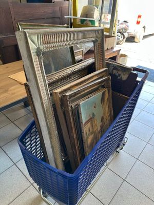 a blue basket filled with framed pictures on the floor