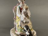 une figurine représentant une femme assise sur une chaise avec un chien