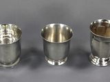 trois tasses en argent posées l'une à côté de l'autre sur une table