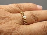 a woman ' s hand holding a gold ring with a pearl on it