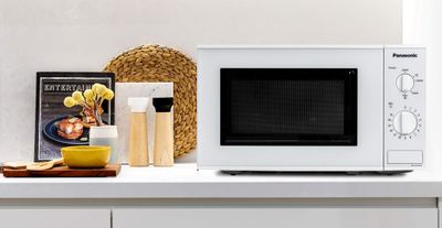 a microwave sitting on a white counter top with a magazine on it