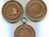 Trois médailles anciennes en bronze sont exposées sur un fond blanc