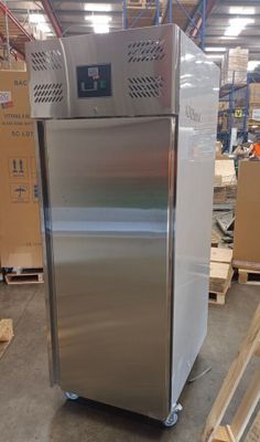 a silver refrigerator in a warehouse with boxes and pallets in the background