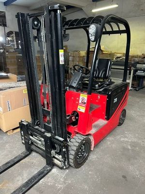 un chariot élévateur rouge garé dans un entrepôt, avec des cartons par terre