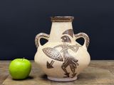 a vase with a design on it next to a green apple