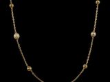 a gold necklace with pearls on a black background