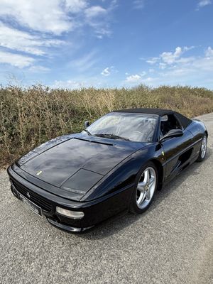 une voiture de sport noire garée sur le bord de la route, devant un champ