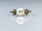 a close up of a pearl and diamond ring on a white surface