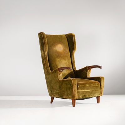 un fauteuil à oreilles en velours vert, avec une structure et des accoudoirs en bois