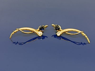 paire de boucles d'oreilles dorées ornées de pierres noires et blanches sur fond bleu