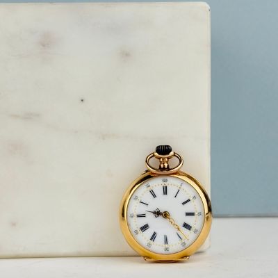 une petite montre de poche en or posée sur un bloc de marbre