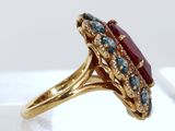 an image of a gold ring with a red stone surrounded by blue and white diamonds