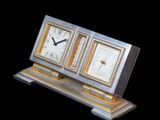 une horloge argentée et dorée posée sur un socle, sur fond noir