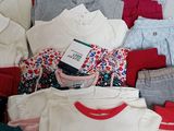 a pile of baby clothes on a bed with a tag on it