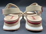 beige sandals with red accents on a grey surface with a black background