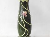 a green vase with pink flowers on it sitting on a table