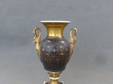 un vase doré et noir posé sur un socle, sur fond gris