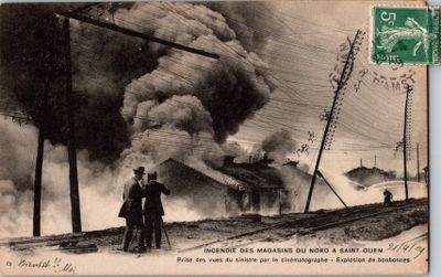 une vieille carte postale représentant deux hommes debout devant un feu d'où s'échappent des volutes de fumée