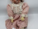 une poupée ancienne assise sur une surface blanche, vêtue d'une robe rose et d'un bonnet