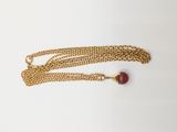 a gold chain with a red bead on it