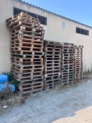 une pile de palettes posée à l'extérieur d'un bâtiment, à côté d'un fût bleu