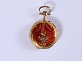 une montre de poche rouge et dorée posée sur une surface blanche