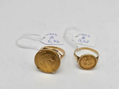 deux bagues en or surmontées d'une pièce de monnaie, posées sur une surface blanche