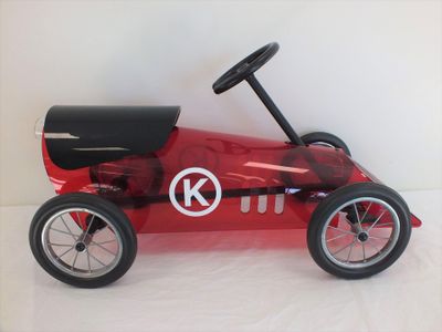 a red pedal car with a steering on a white surface