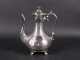 an antique silver tea pot with a bird handle on a black surface