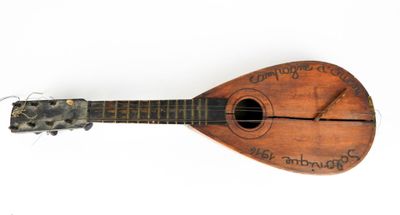 une vieille guitare en bois, sur laquelle figurent des inscriptions, posée sur une surface blanche