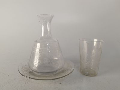un verre et une carafe posés sur une assiette, à côté d'un verre à pied