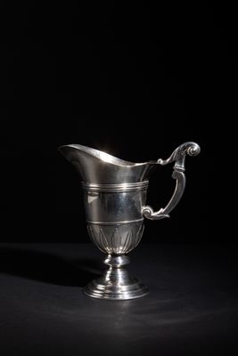 an antique silver pitcher on a black table with a black background