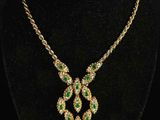 a gold necklace with emerald and white stones on a black mannequin