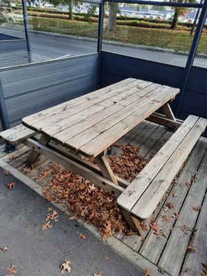 une table de pique-nique en bois sur une terrasse, avec des feuilles par terre