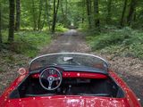a red car driving down a dirt road in the woods