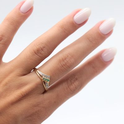 the hand of a woman with a white manicured nails and a gold ring with a green stone