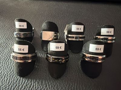 six anneaux noirs et argentés, portant des étiquettes, posés sur une surface en cuir