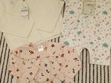 trois vêtements de bébé disposés sur une couverture posée sur un lit