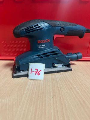 une ponceuse orbitale Bosch posée sur une table, à côté d'une boîte rouge