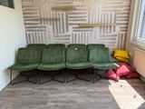 quatre chaises vertes dans une pièce, avec un mur de briques derrière elles