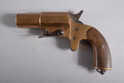un vieux revolver en laiton avec une crosse en bois, posé sur une surface blanche