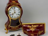 a red and gold clock sitting next to a cup