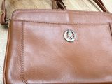 brown leather purse with a silver logo on it sitting on a wooden surface