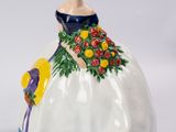 une figurine représentant une femme vêtue d'une robe et tenant un bouquet de fleurs