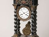une horloge noire et dorée posée sur un socle, sur fond blanc